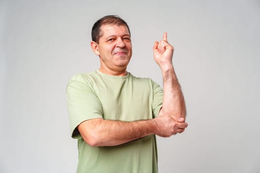 A middle-aged man with a thoughtful expression gestures with one finger raised while standing against a plain background close up