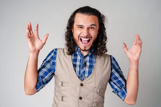 A man with curly hair excitedly gesturing while wearing a plaid shirt and vest against a plain background close up