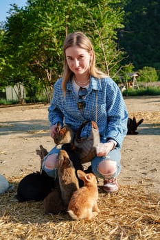 Young woman enjoys playful moments with a group of rabbits at a tranquil farm during a sunny afternoon close up
