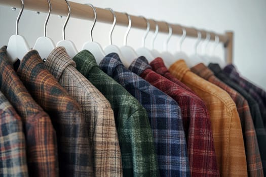 Collection of plaid flannel shirts in various colors hanging on wooden rack, autumn and winter casual fashion wardrobe essentials.