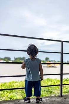 A little boy stands near the river and looks at the water.