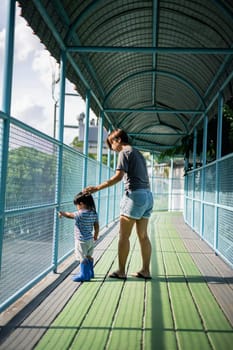 Mother and son looking animal  in an outdoor zoo. They are standing next to a cage with animals.