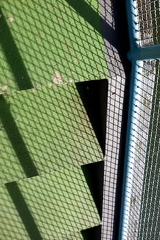Looking down some green concrete stairs. The shadow of the handrails on the stair.