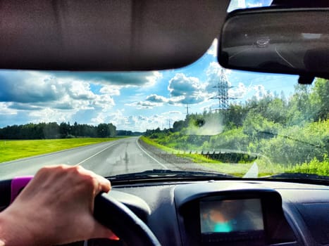 The driver steers along highway, with vibrant green fields and dramatic clouds stretching across the sky
