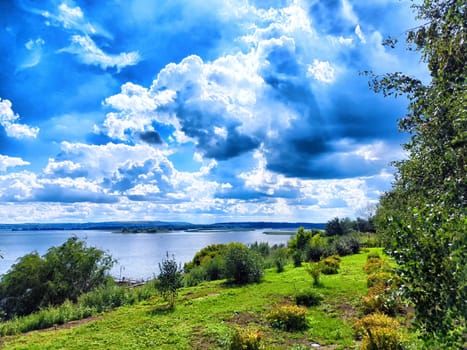 The view reveals lush greenery lining a riverbank under a stunning blue sky filled with clouds.