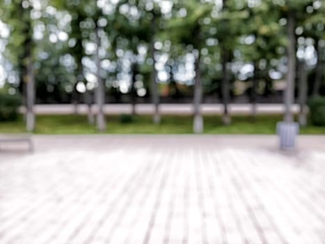 The scene captures a serene park area with lush trees providing shade along a spacious trail, perfect for walks. Blurred picture