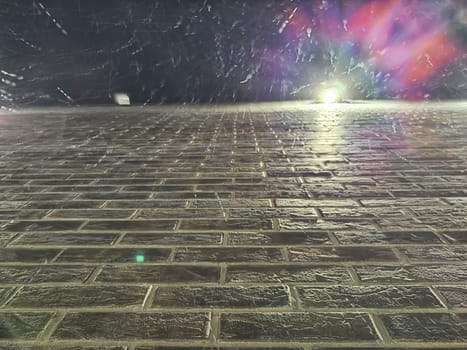 Droplets of water cascade down a brick wall illuminated by soft lights at night.