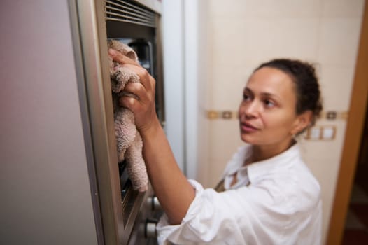 A woman diligently cleans the oven in her kitchen, emphasizing cleanliness and home hygiene. Her focused expression reflects dedication to maintaining a pristine cooking environment.