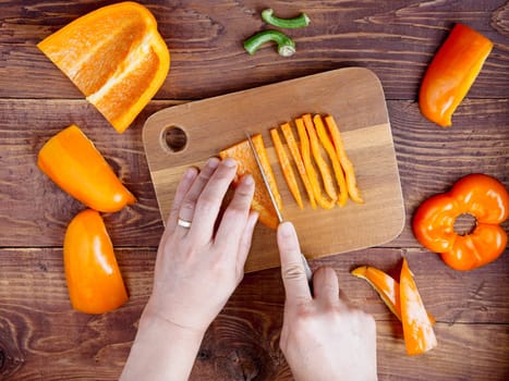 A flatlay photo of hands cutting orange bell peppers in a studio setting.