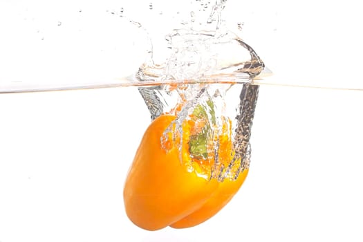 A large orange bell pepper making a splash after being dropped in water in this studio photo.