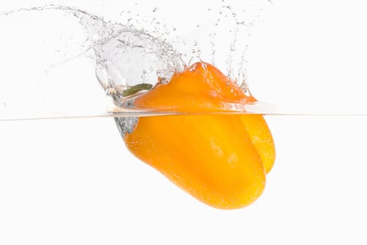 A large orange bell pepper making a splash after being dropped in water in this studio photo.
