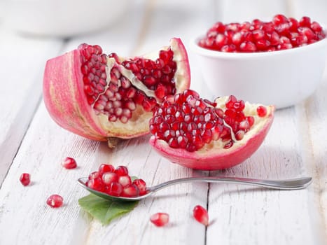 A close up vivid photo of opened pomegranates and their seeds on a spoon and in a bowl.