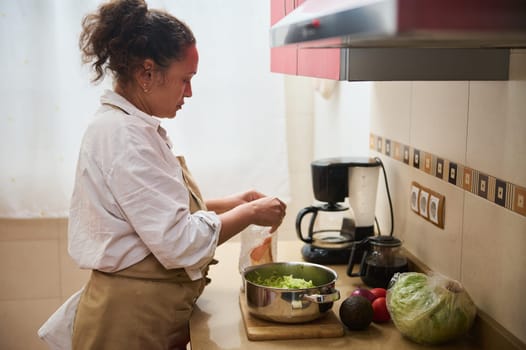 Woman in a cozy kitchen setting, preparing a healthy green salad with fresh vegetables. The scene is calm and domestic, emphasizing home-cooked meals and healthy eating.