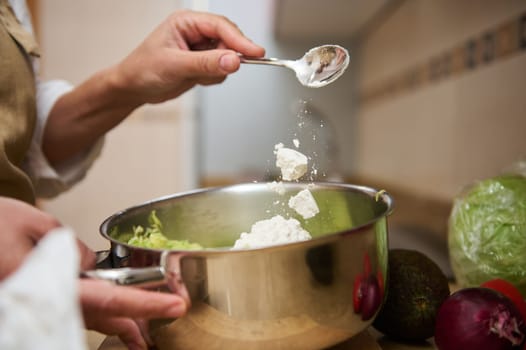 Close-up of hands adding seasoning to a pot filled with fresh vegetables. The image captures the essence of cooking preparation in a home kitchen, emphasizing freshness and culinary creativity.