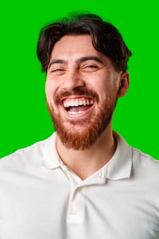 A smiling young man with a beard poses against a bright green background close up