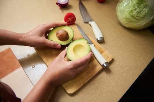 A person slices an avocado on a wooden board in a kitchen, surrounded by ingredients. The scene is vibrant, emphasizing healthy eating and food preparation. Ideal for culinary themes.