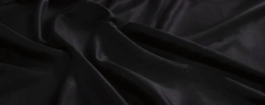 A luxurious black fabric lies gracefully on a surface, showcasing its smooth texture and subtle sheen in a dimly lit environment, adding elegance and depth to the composition.