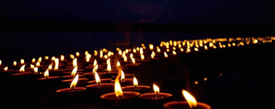 A long line of flickering candles illuminates the riverbank as twilight descends, creating a serene and peaceful atmosphere.