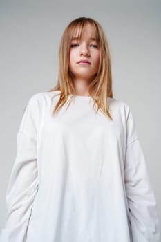 Young woman with long hair in a white sweatshirt standing against a light gray background close up
