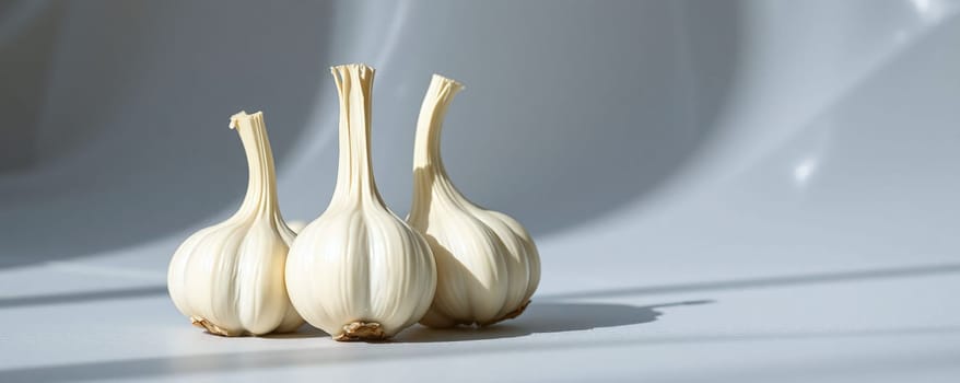 Three fresh garlic bulbs are placed on a smooth light surface. The natural sunlight casts soft shadows, highlighting their unique shapes and textures, creating a tranquil atmosphere.