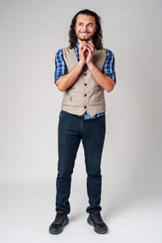 Man in a plaid shirt and vest stands smiling, looking optimistic in a neutral studio setting close up