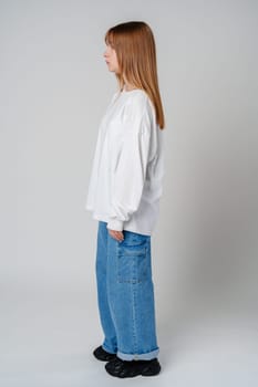 A young woman stands side profile, showcasing a casual outfit with a white oversized shirt and blue wide-leg jeans