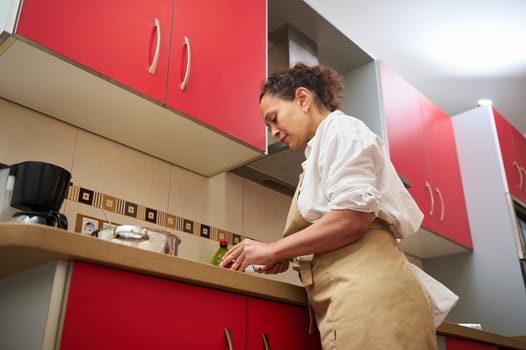 Woman cooking in a contemporary kitchen, focusing on meal preparation with red cabinets and modern appliances. Casual home cooking atmosphere.