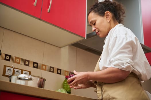 A woman focused on cooking in a modern kitchen with red cabinets. She is peeling vegetables, showcasing a peaceful domestic scene with emphasis on home-cooked meals and culinary skills.
