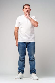 A man makes a playful gesture with his hand near his mouth while smiling in a neutral backdrop close up
