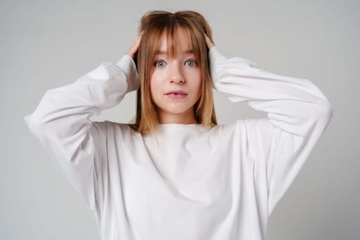 A young woman with light brown hair and blue eyes expresses surprise in a minimalist studio setting