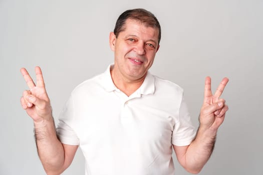Man wearing a white shirt making peace signs with his hands against a plain background close up