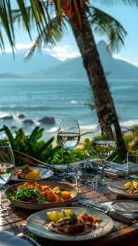 A table is set with plates of food and wine glasses overlooking the ocean. The view includes water, sky, coastal landforms, beach, and trees, creating a beautiful natural landscape perfect for travel