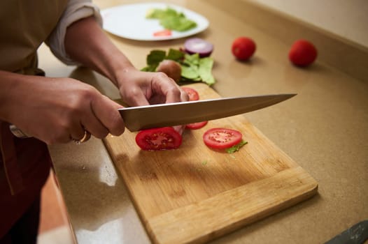 A close-up view of a person slicing fresh tomatoes on a wooden cutting board in a kitchen. The image captures the precision and care in the culinary process, complemented by vibrant colors.