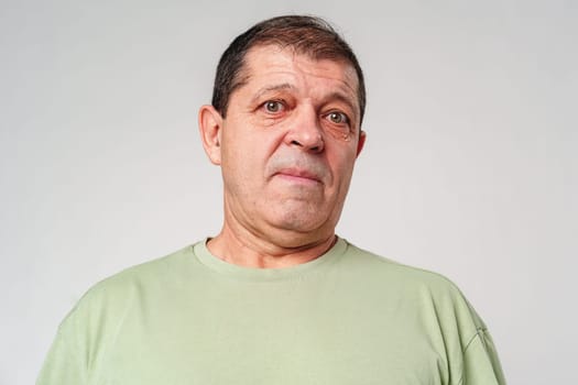 Friendly older man smiling warmly in a light green shirt against a neutral background close up
