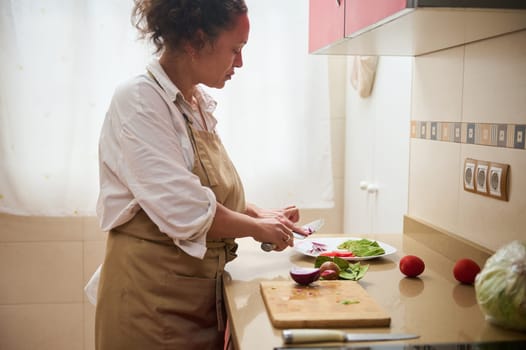 A woman in an apron skillfully chops fresh vegetables in a contemporary kitchen. Natural light and peaceful cooking moments create a calm and focused atmosphere.