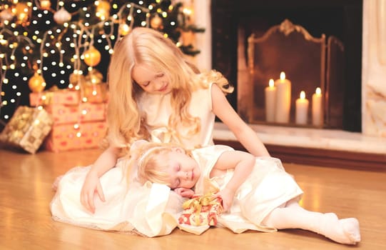 child little girl gives a gift box to sister over christmas tree and  fireplace at home