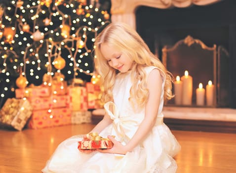 child little girl with gift box near christmas tree and fireplace at home