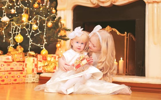 children little girls with gift boxes near christmas tree and fireplace at home