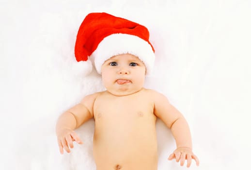 Christmas and family concept - cute funny baby in red santa hat lying on white bed at home, humor, joke