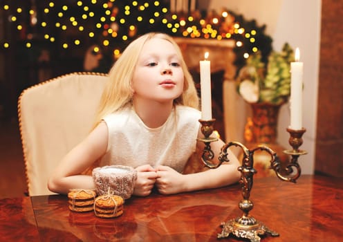 Christmas child blowing on candle makes a wish sitting at the table home