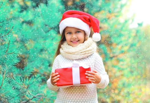 Christmas child little girl in santa red hat with gift box near branch tree