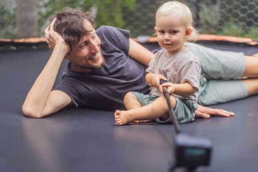 Dad and toddler sitting on an outdoor trampoline with an action camera. Family bonding, playful moments, and outdoor fun concept.
