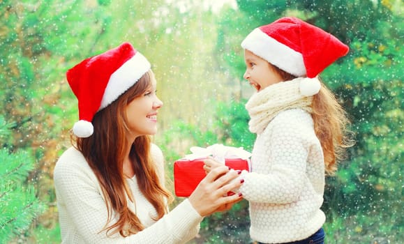 Christmas family child and mother in santa red hat with box gift over a tree