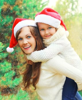 Christmas family child hugging mother in santa red hats together over a tree having fun