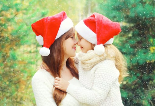 Christmas family child hugging mother in santa red hats together over a tree