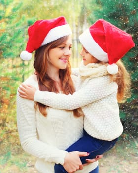 Christmas family, child hugging mother in santa red hats together over a tree having fun