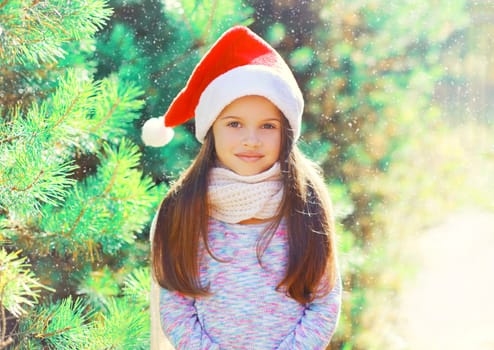 Christmas portrait child little girl in santa red hat near a tree