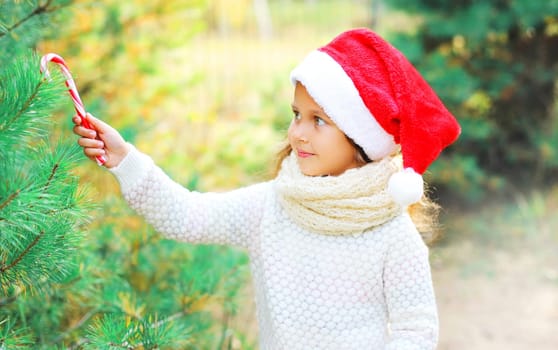 Christmas smiling child little girl in santa red hat decoration sweet lollipop cane to branch tree