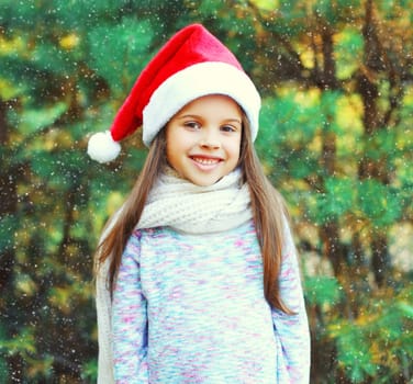 Christmas smiling child little girl in santa red hat over a tree