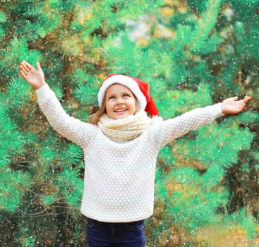 Christmas smiling child little girl in santa red hat over a tree having fun
